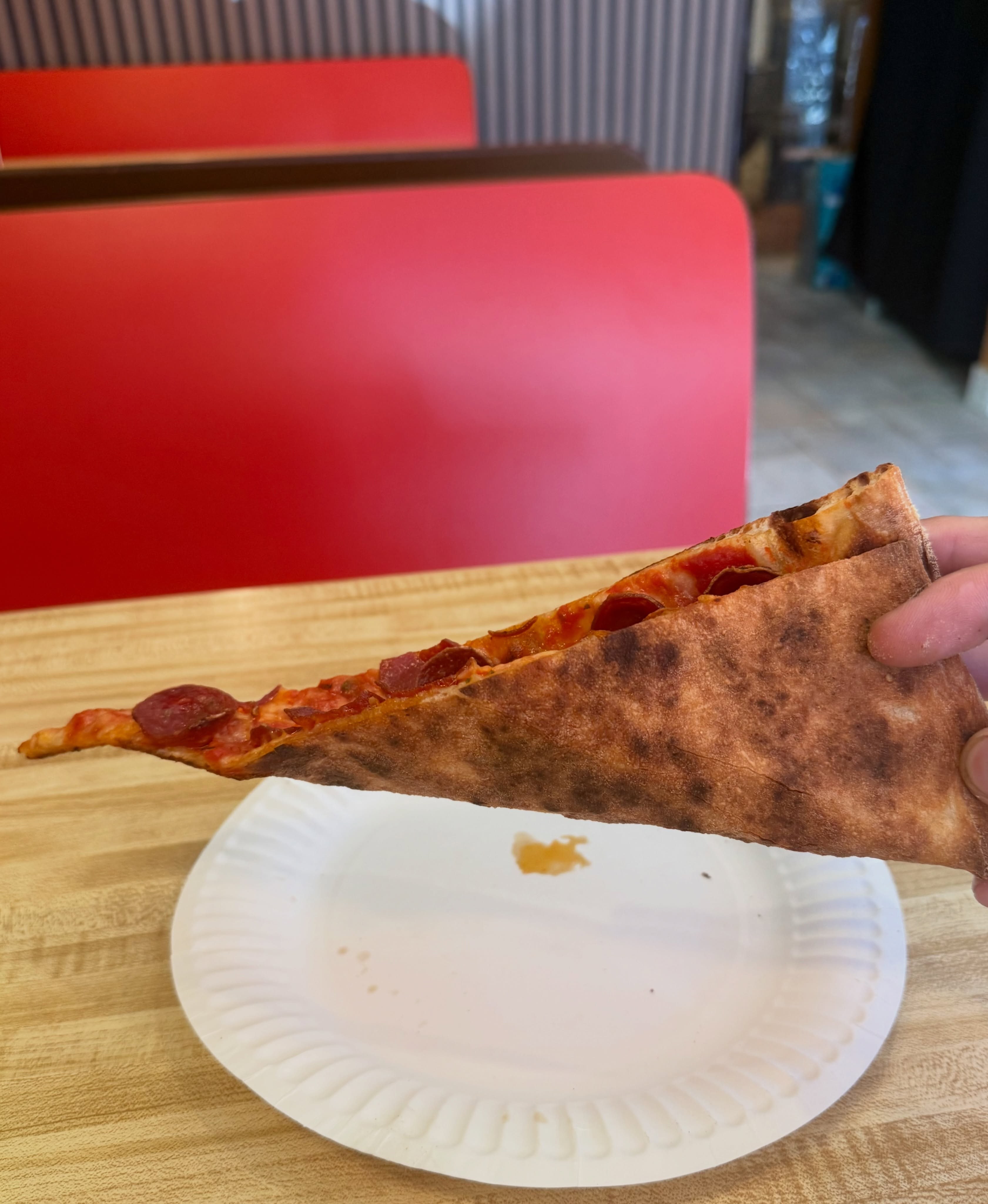 Slice held up showing its thin profile, Andrea’s Pizza
