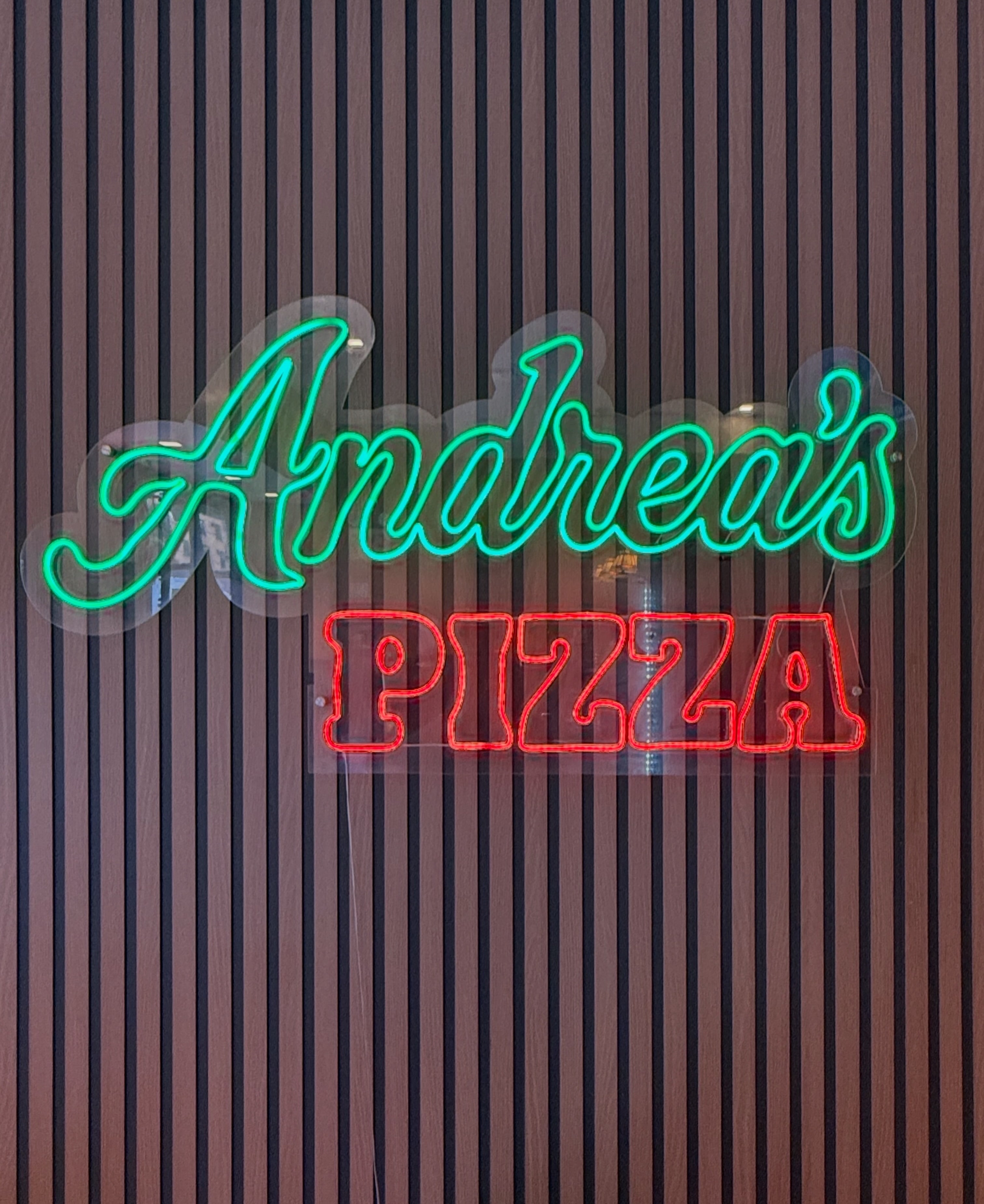 Neon sign reading Andrea’s Pizza above the counter