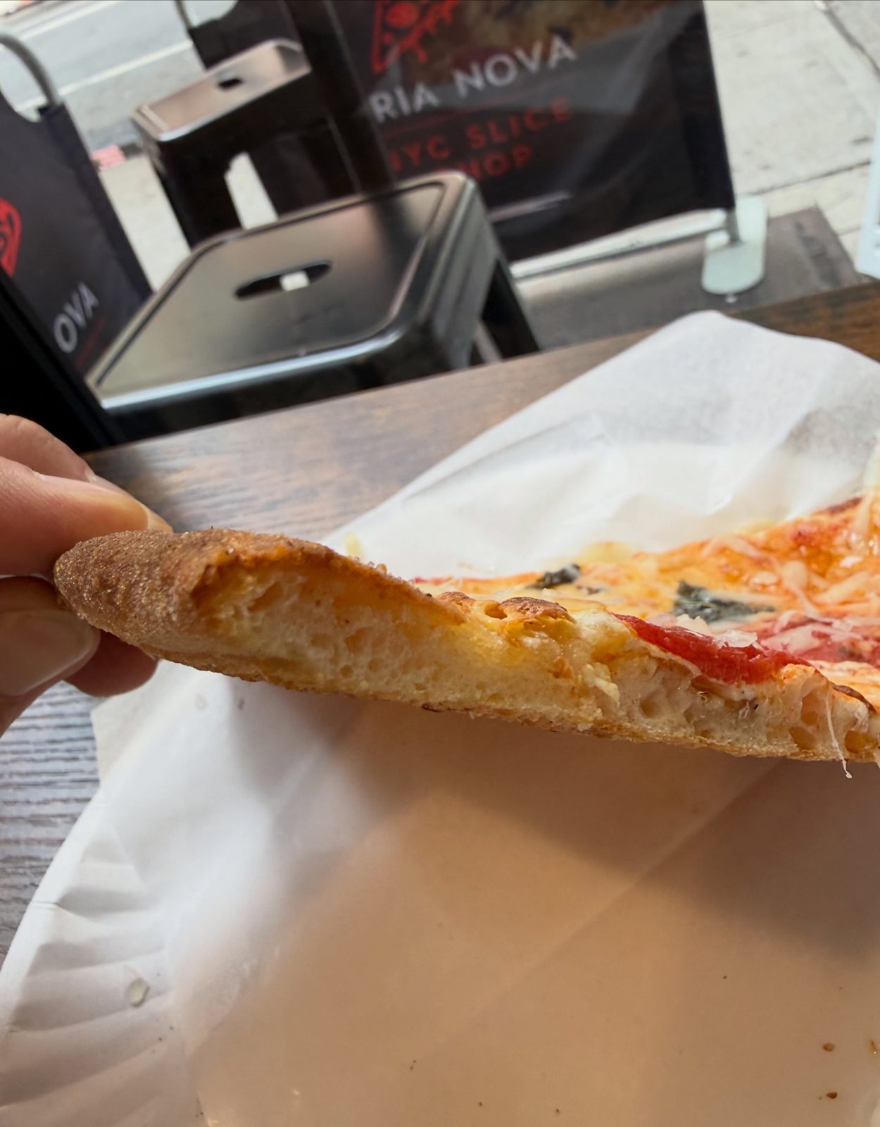 Cut edge of the Aria Nova slice showing an open, aerated crumb beneath a thin layer of sauce and cheese