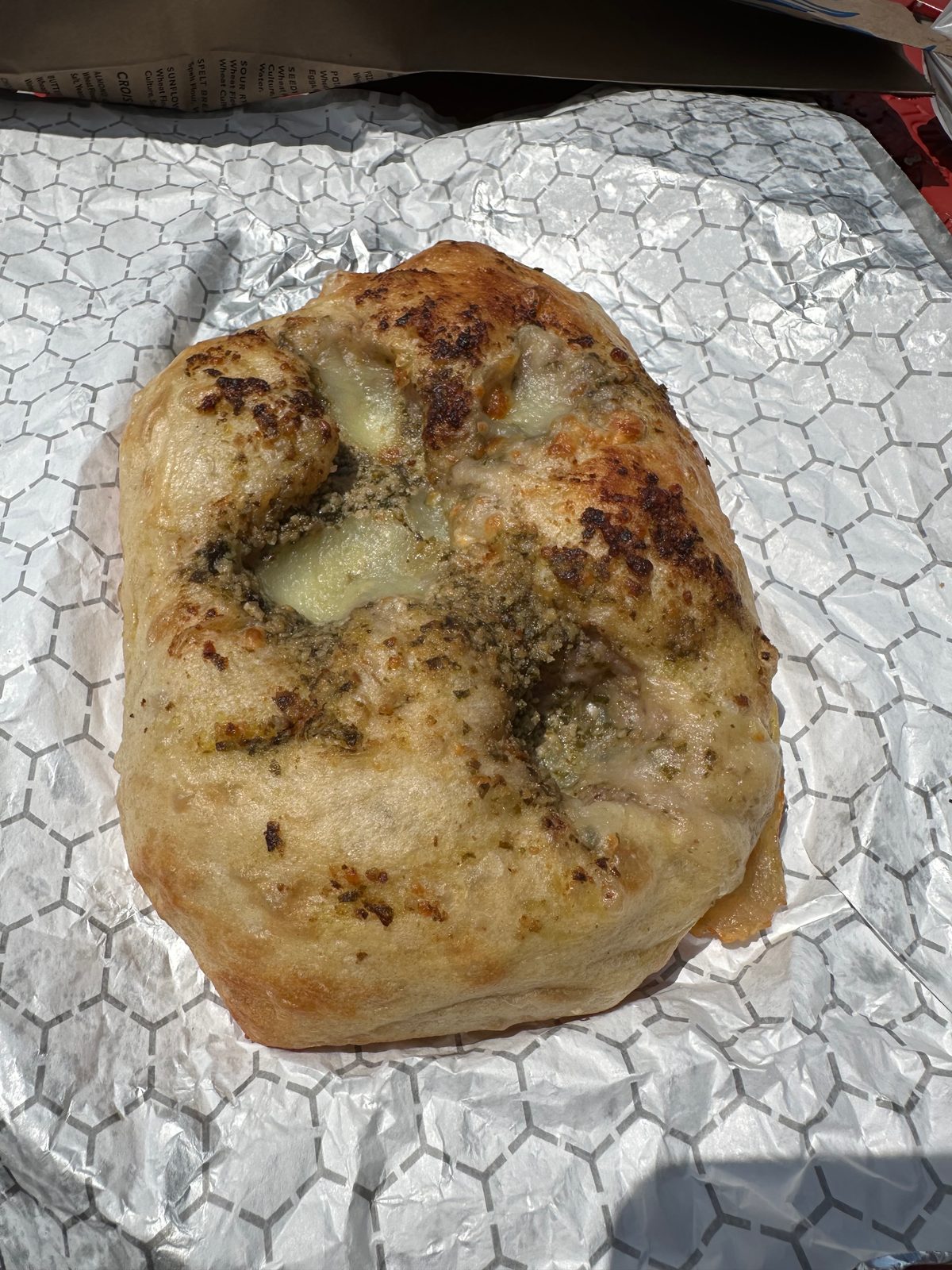 Thick focaccia square topped with pesto and melted cheese on foil, Blue Oven Bakery