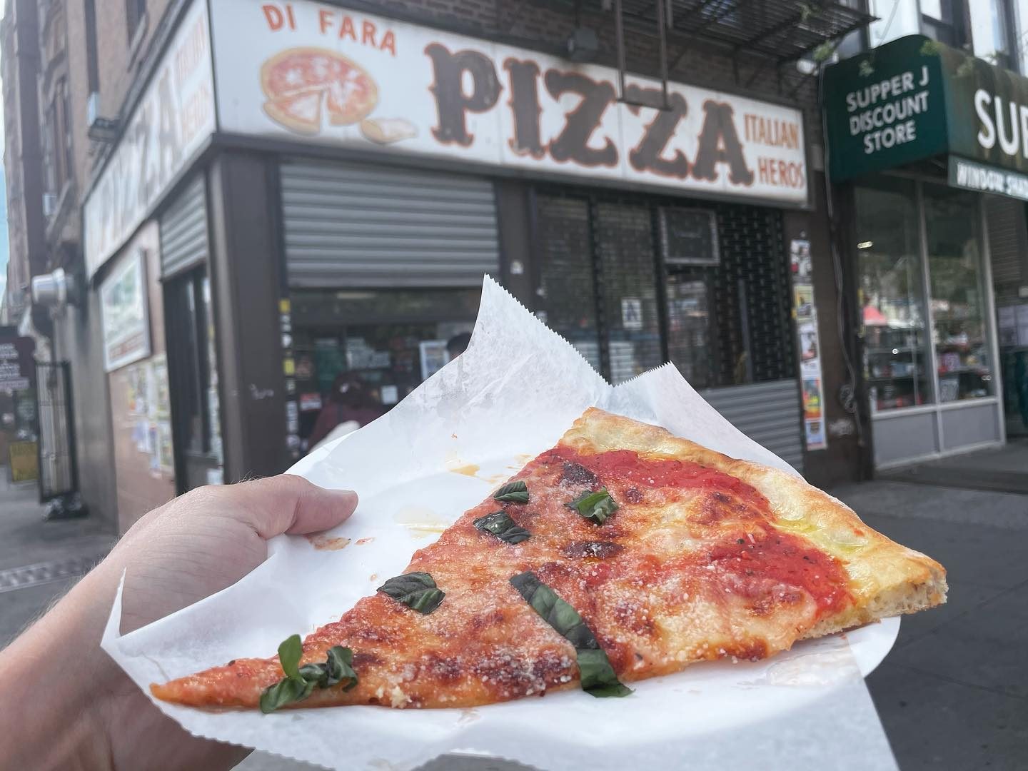 Slice held up in front of the storefront at Di Fara Pizza