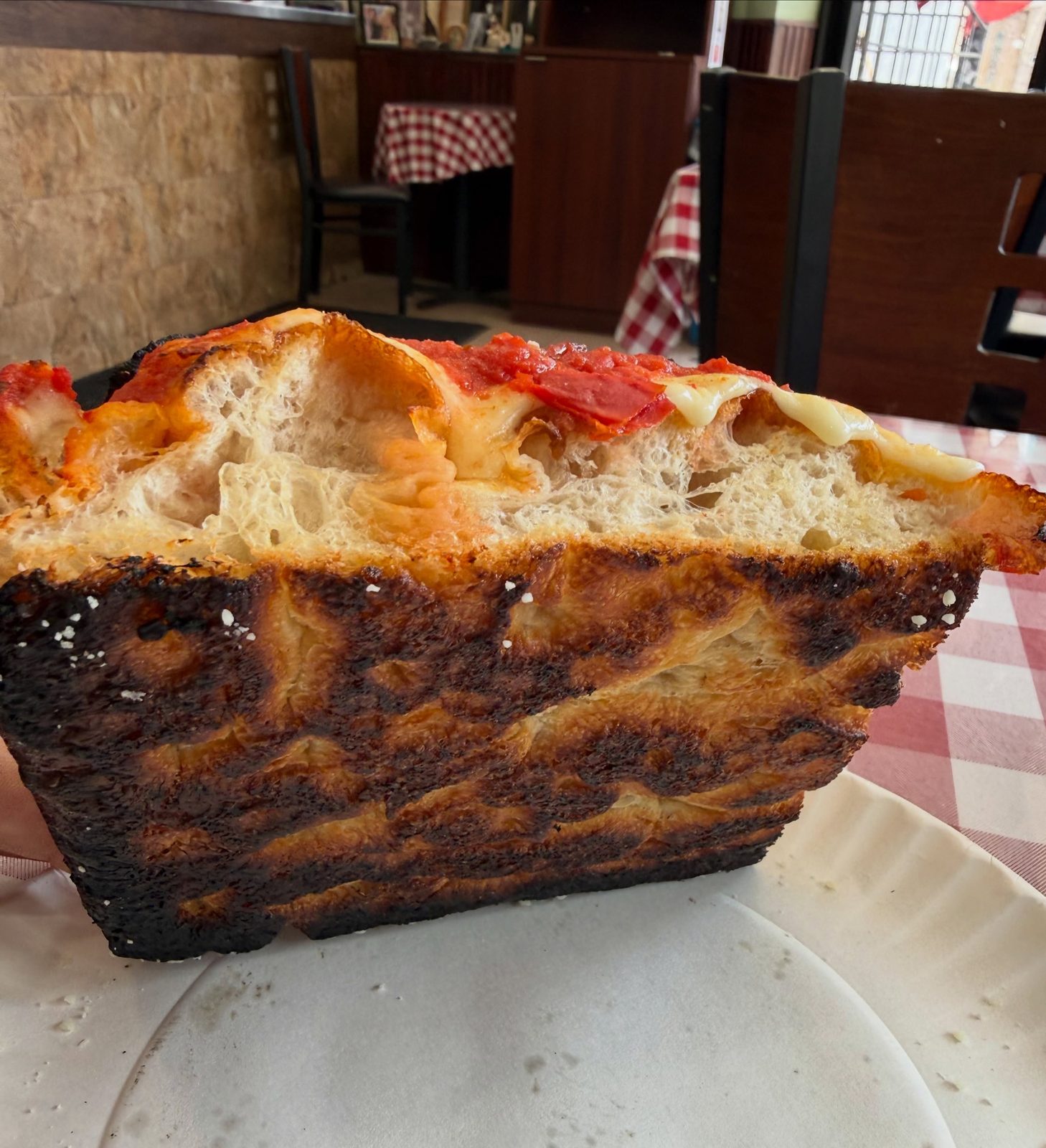 Side profile of the Sicilian slice showing its charred, deeply browned bottom at Mano's Pizza