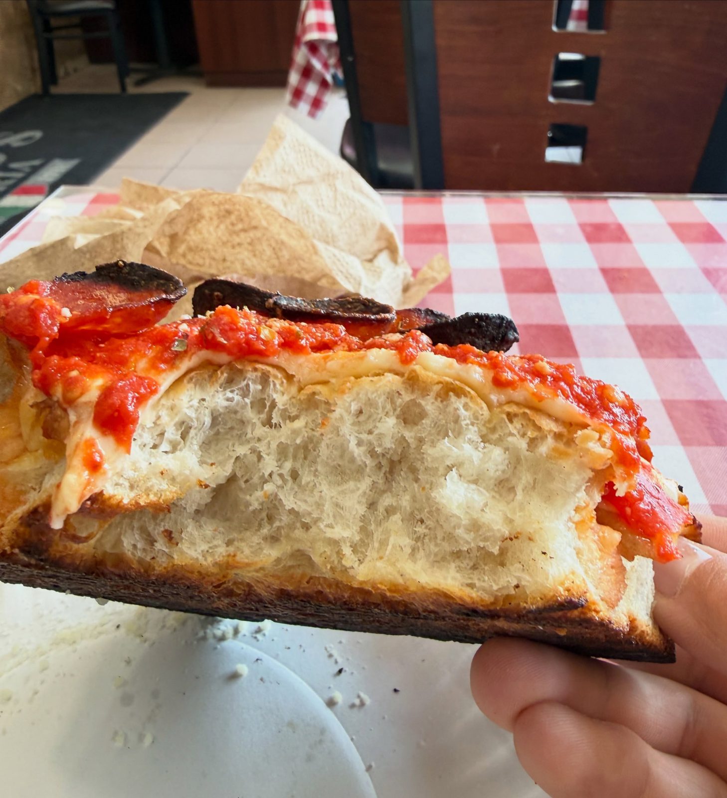 Airy, open crumb inside a Sicilian slice held up at Mano's Pizza