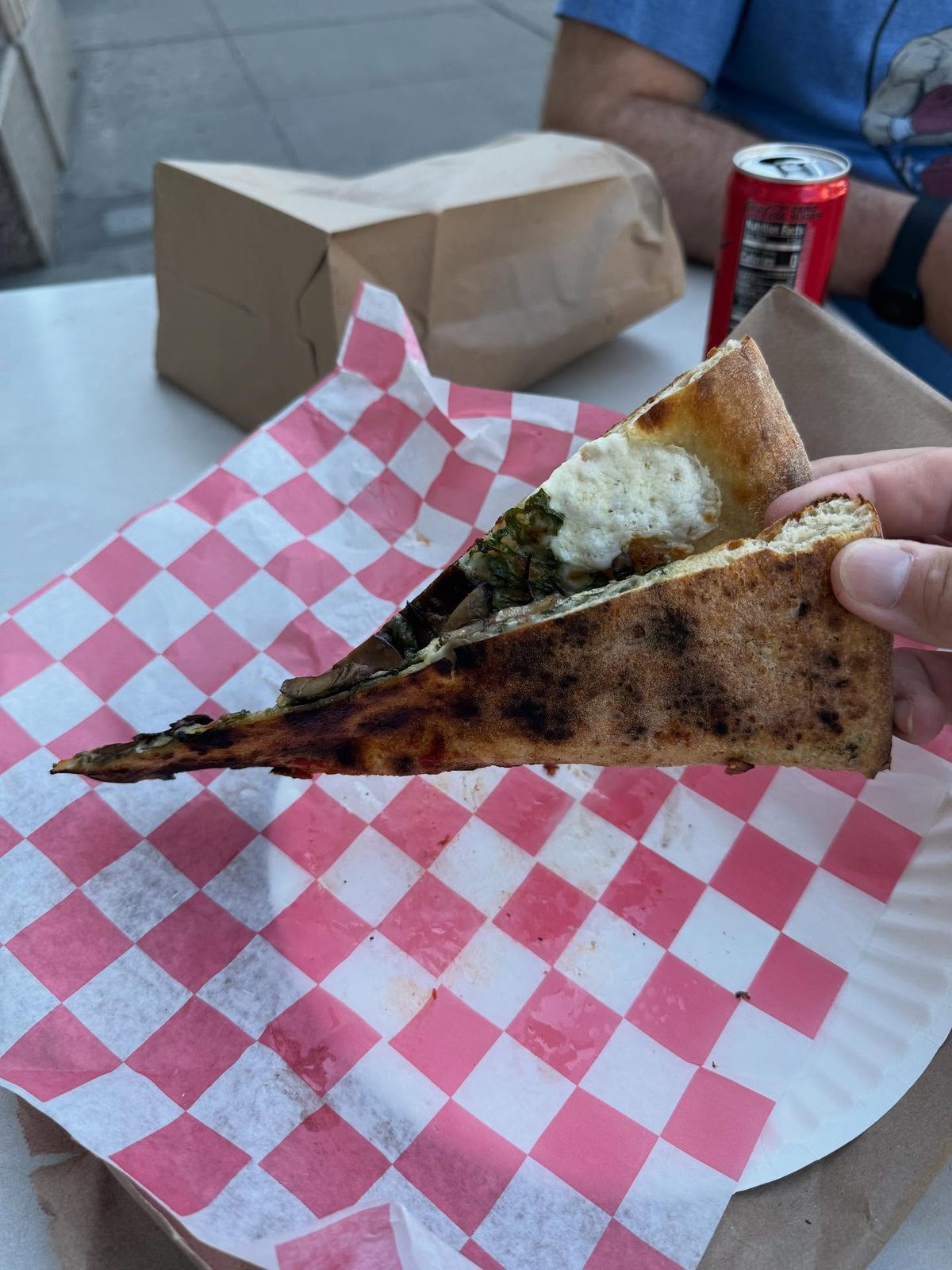 Thin slice held up to show its crisp, lightly charred crust at Norm’s Pizza