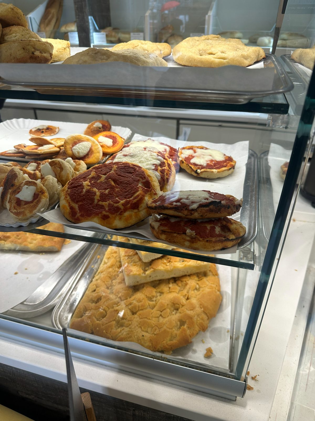 Bakery display case holding cecina alongside focaccia and small tomato pizzette, Pane & Vino dal Piova