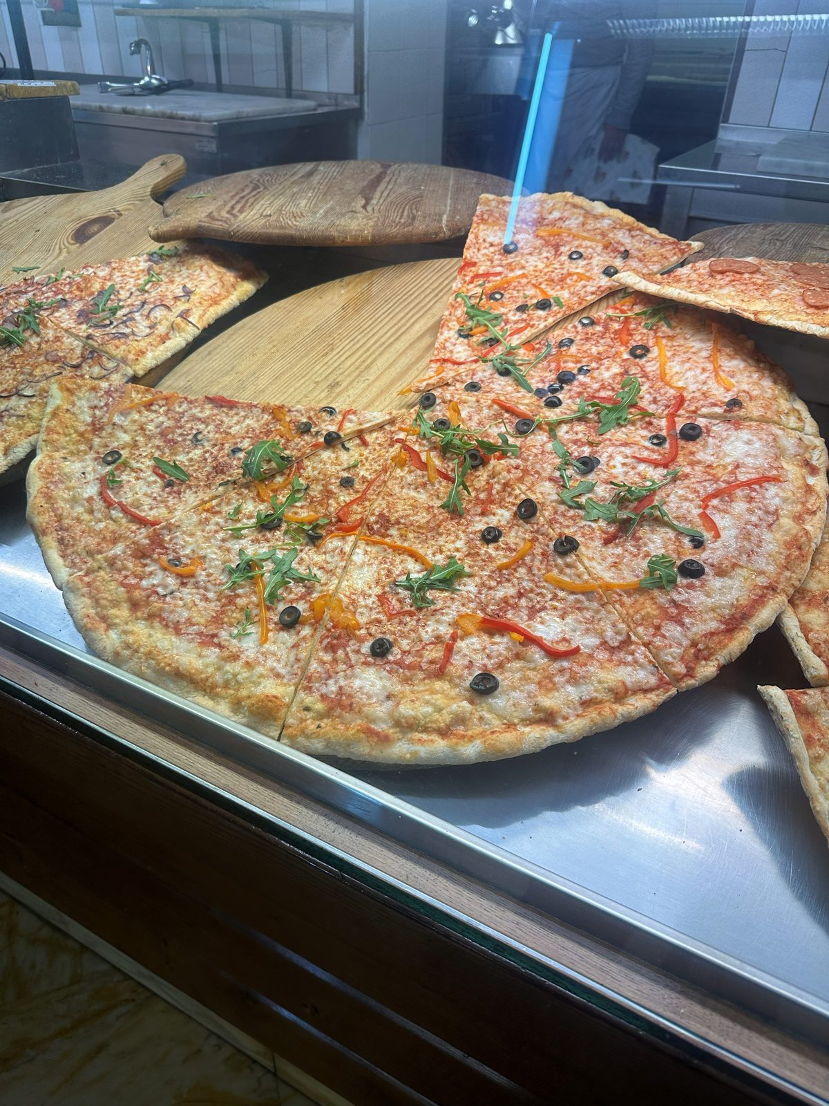 Whole thin pies on wooden boards in the counter display, Pizza Al Volo