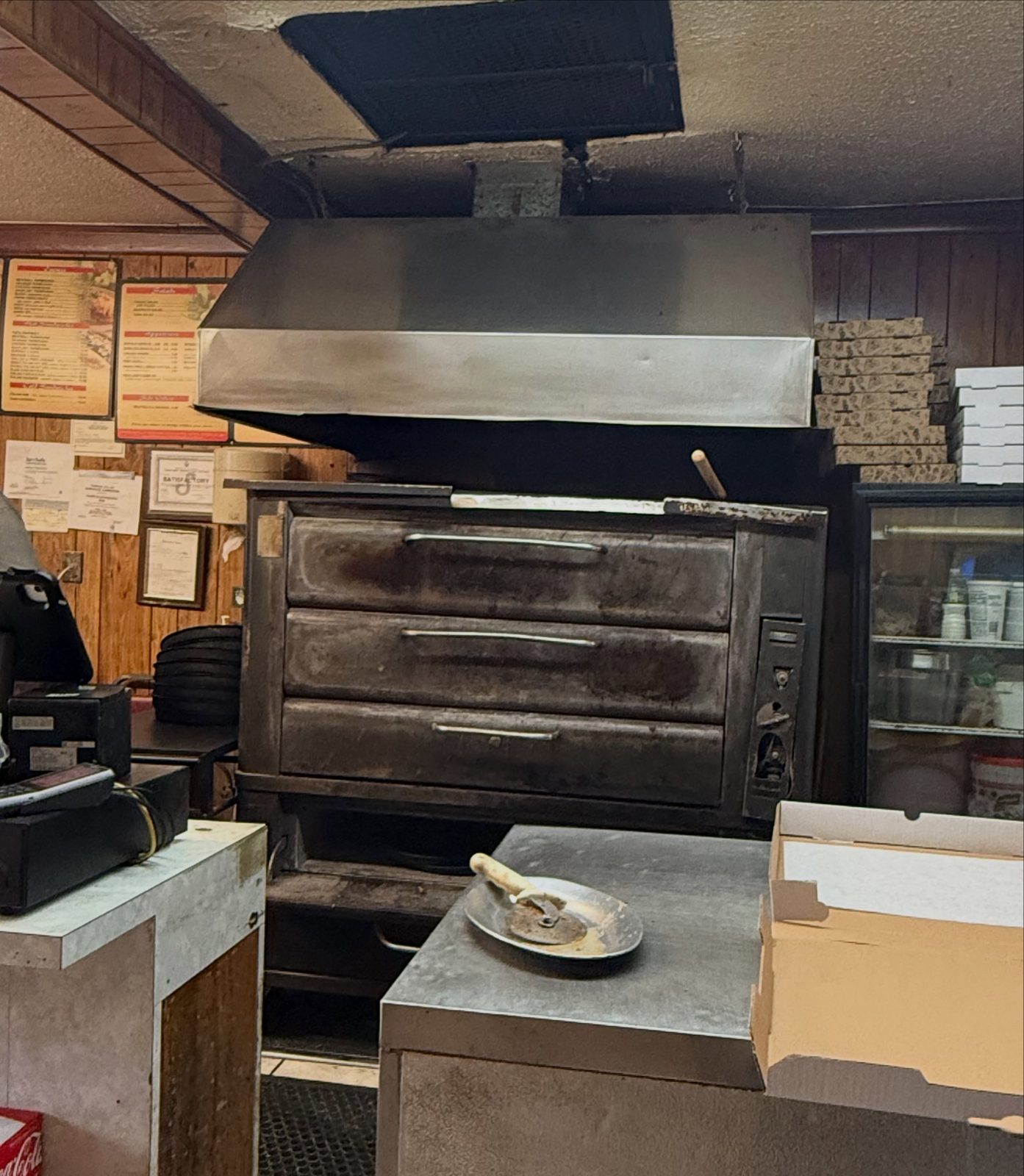 The battered old deck oven behind the counter at Pizza Land, under wood panelling and menu boards