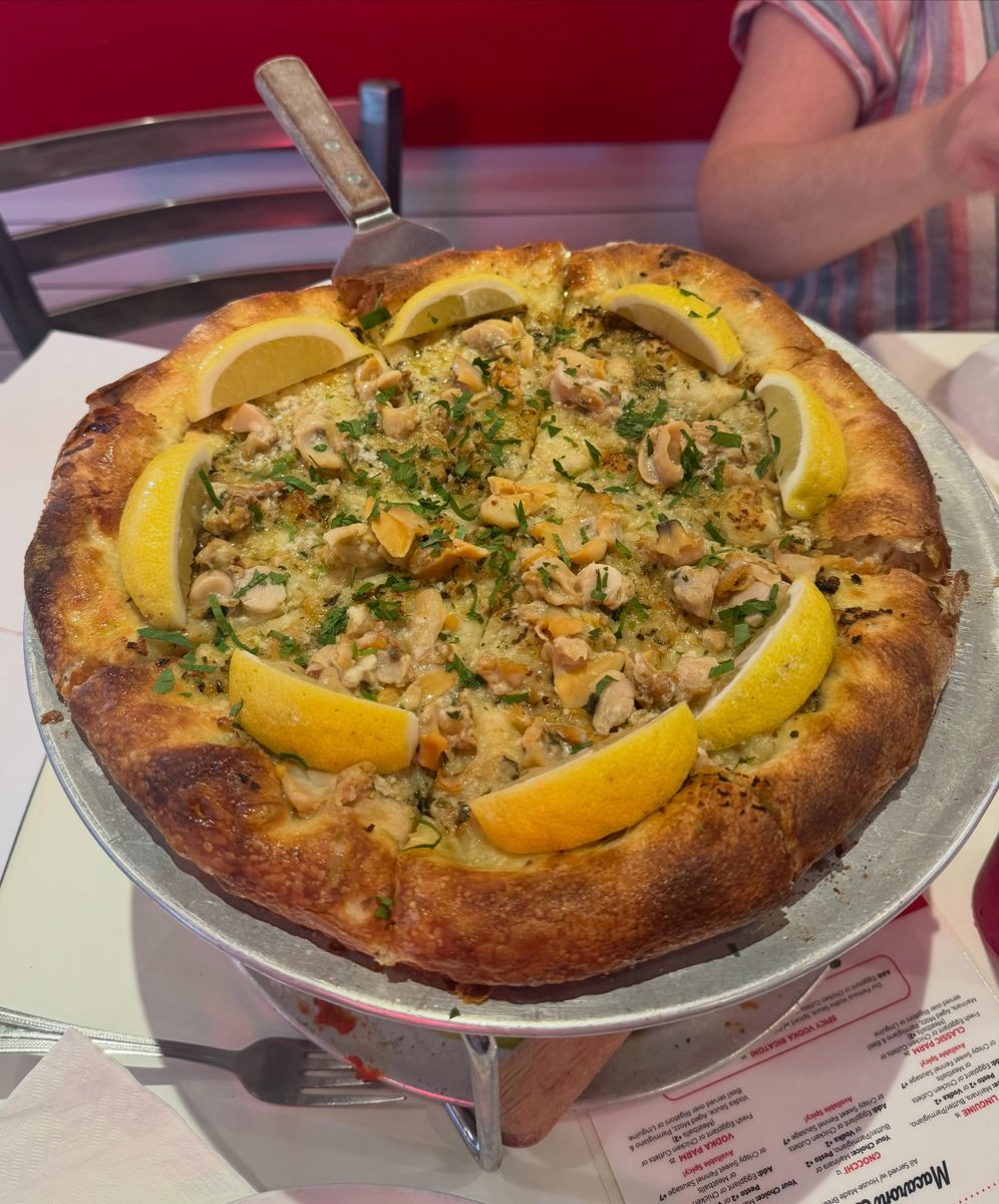 Whole clam pie on a raised pan at Andrew Bellucci’s Pizzeria, lemon wedges around the rim