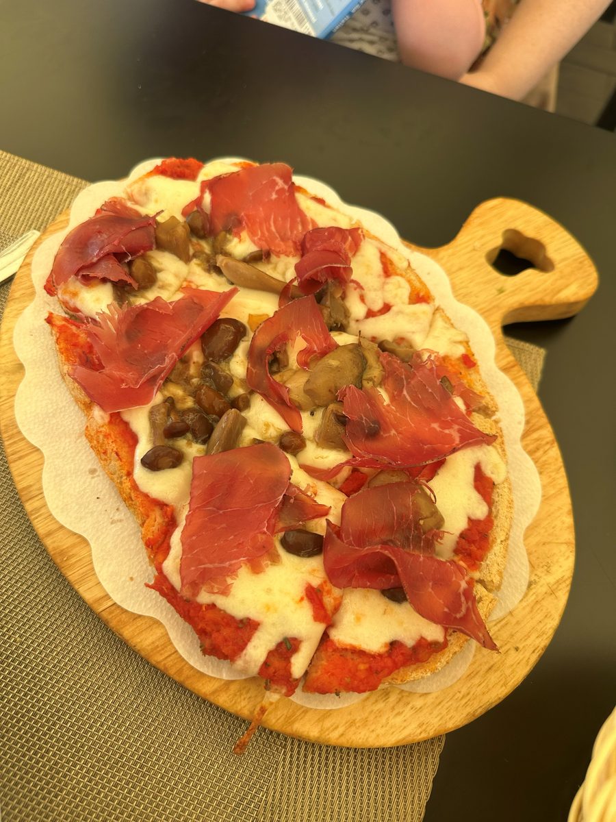 Thin round pie on a wooden board topped with cured ham, mushrooms and mozzarella, Caffè Le Logge