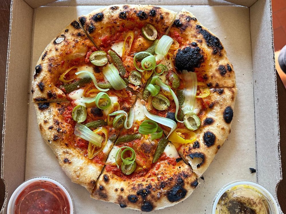 Boxed pie topped with cornichon curls and green olives, Companion Pizza