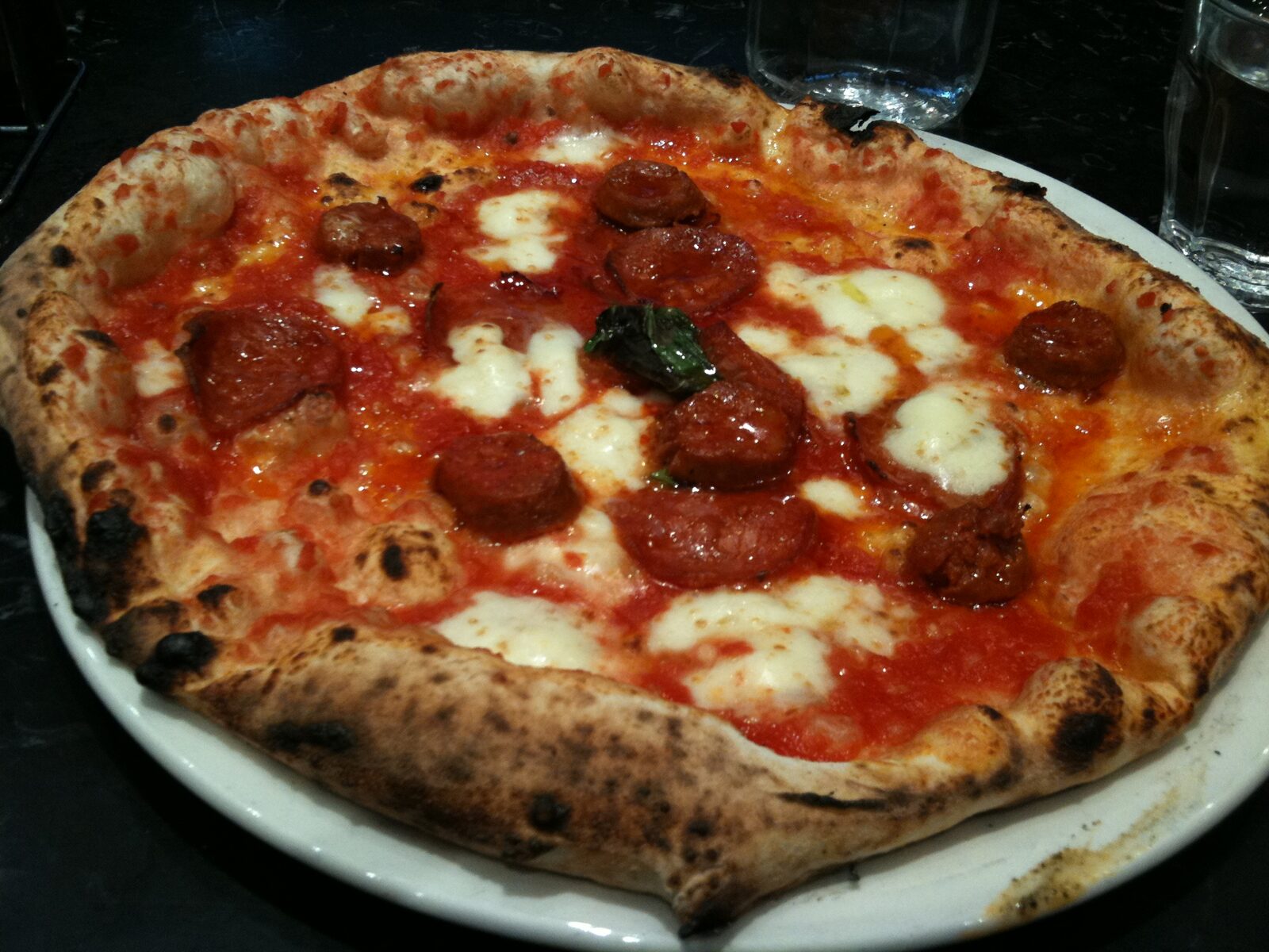 Leopard-spotted Neapolitan pie with cured sausage rounds and basil, Franco Manca