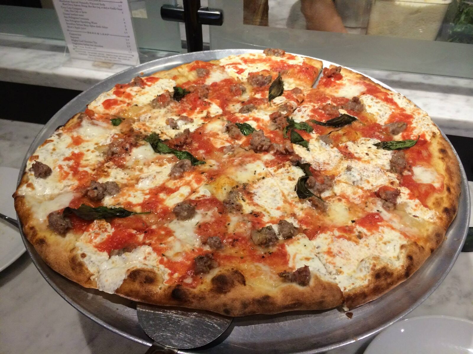 round pie topped with sausage crumbles and scattered basil, Juliana's