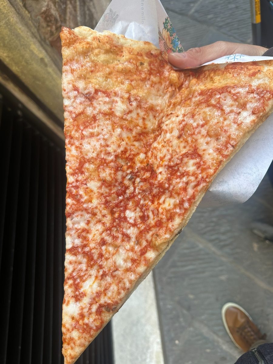 Large thin triangular slice held up on paper in the street, Pizza Al Volo