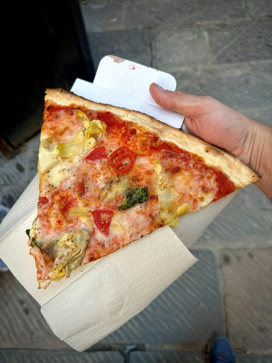 Wide triangular slice with tomato, mozzarella and greens held on paper, Ricca Pizza